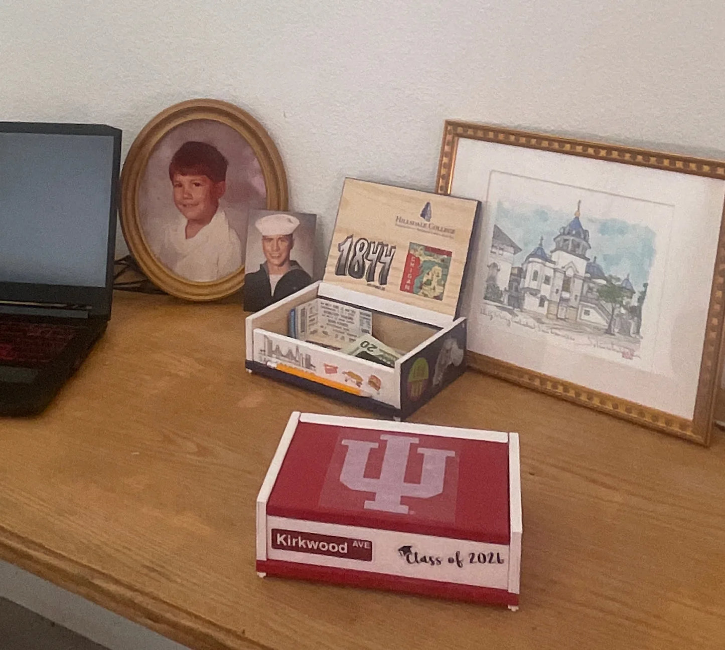 Indiana University keepsake box displayed on a desk beside an open Hillsdale College keepsake box with photographs and memorabilia.